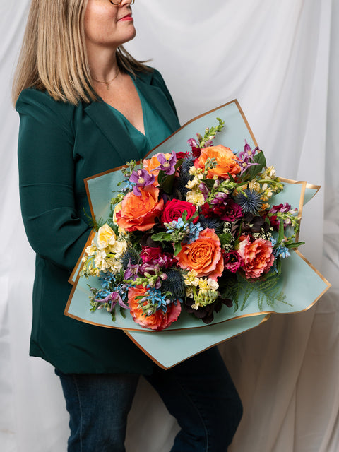 Person holding a colorful bouquet of flowers in a decorative light blue paper wrapping against a white background