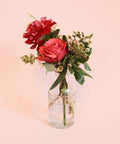 small floral arrangement in a glass bottle style bud vase on a pink background