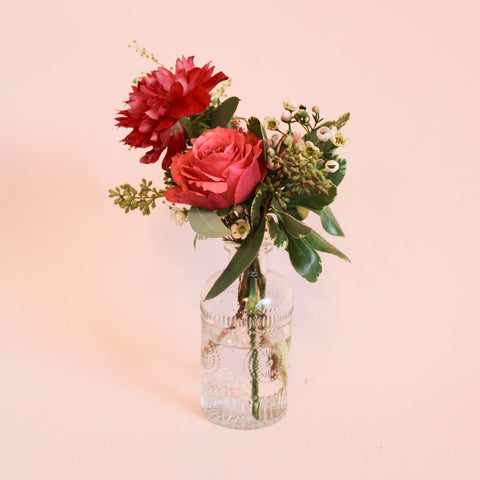 small floral arrangement in a glass bottle style bud vase on a pink background
