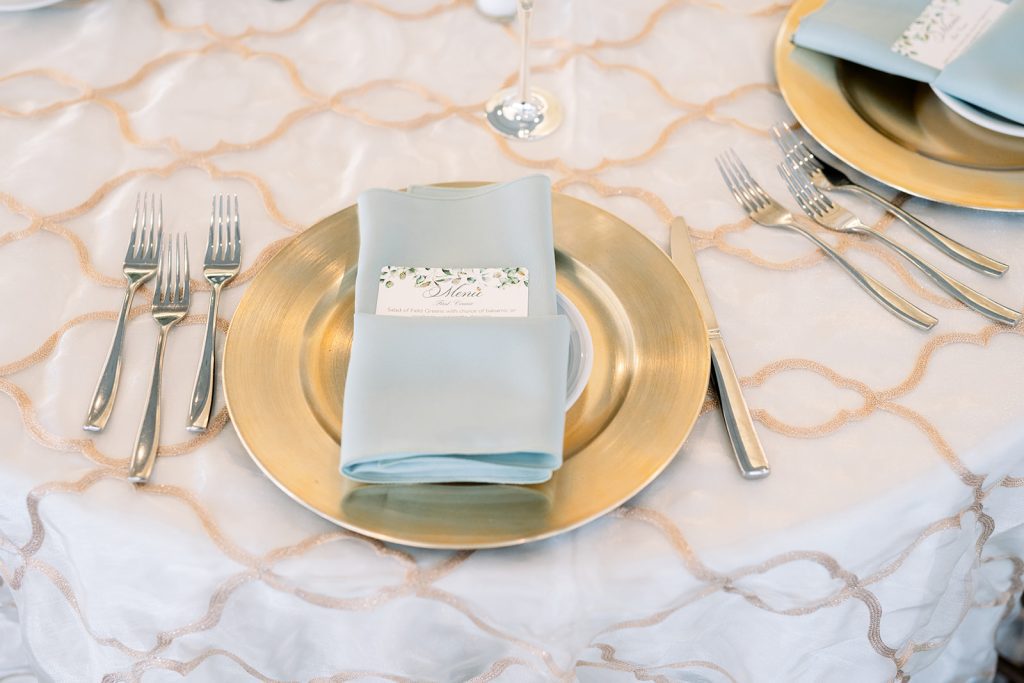 bright elegant summer wedding reception place setting with soft blue napkin and gold charger